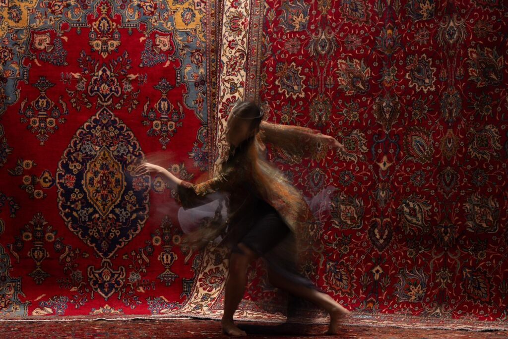 2391db64-ec1a-449e-b12d-2bd5dc76bbca Traditional dancer performing with a beautiful oriental rug from Musee LTD Oriental Rugs Houston as the backdrop, in collaboration with Ashkan Image, showcasing the fusion of art and culture.